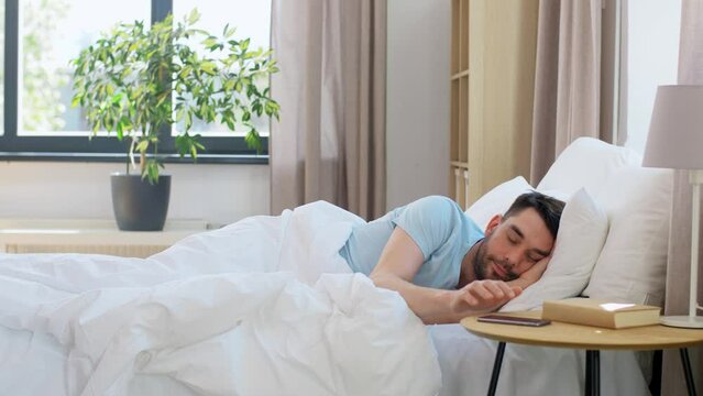 People, Bedtime And Rest Concept - Man Sleeping In Bed And Checking Time On Smartphone At Home