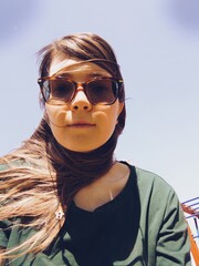 Young slightly smiling woman in sunglasses selfie. Summer long hair girl portrait with blue sky.