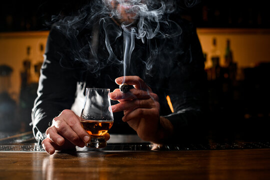 Gorgeous view of male hands holding a glass of alcoholic drink and smoking cigar