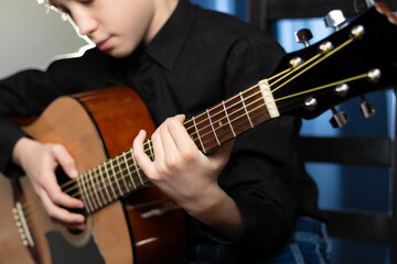 A teenager guy in a black shirt plays the acoustic guitar at a concert on a blue background. Hobby. Musical instruments. Selective focus. Portrait