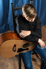 A teenager guy in a black shirt with an acoustic guitar on stage after a concert on a blue...