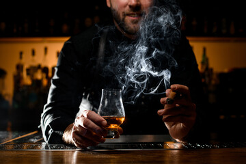 wonderful view of male hands holding a glass of alcoholic drink and smoking cigar