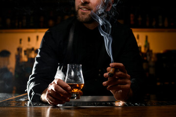 glorious view of male hands holding a glass of alcoholic drink and smoking cigar - obrazy, fototapety, plakaty
