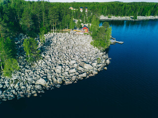 Aerial top view of red log cabin or cottage with a sauna in a green forest near a lake with rocky...