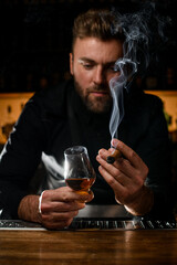 handsome male bartender holding a glass of alcoholic drink and smoking cigar