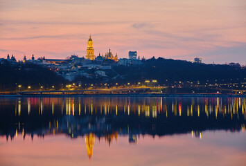 Fototapeta na wymiar Kiev-Pechersk Lavra and city lights. Silhouette panorama at sunset of the colorful sky over the Dnieper river with passing ducks in Kyiv