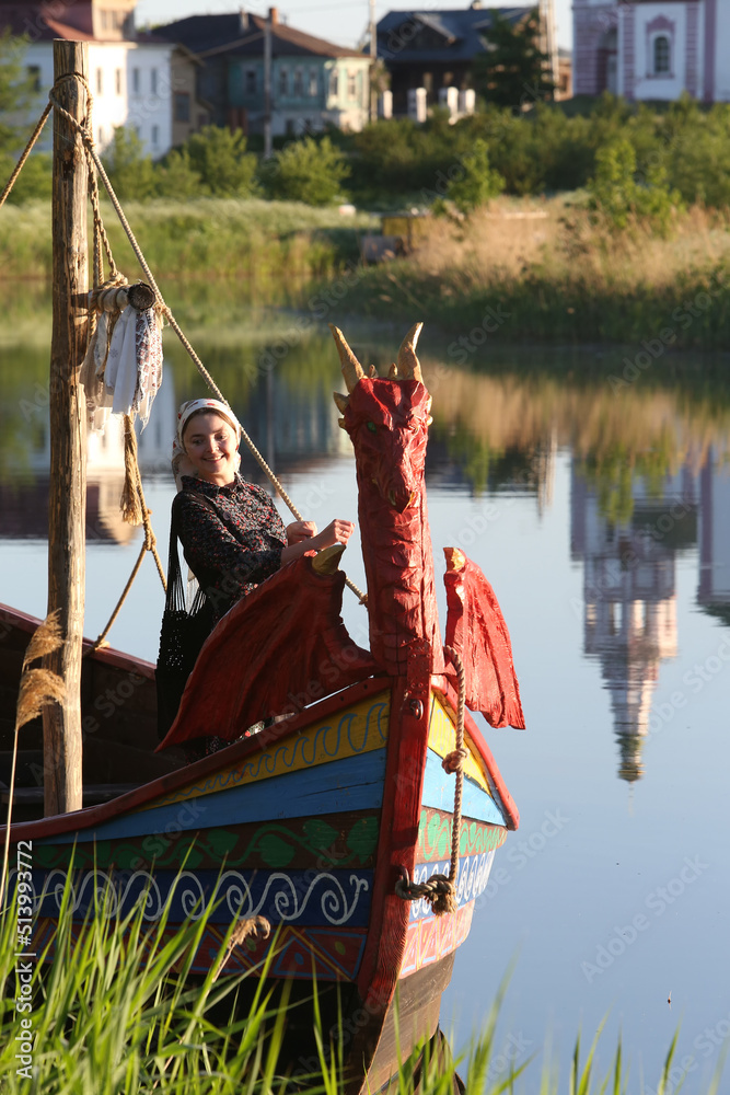 Wall mural Russian tourist woman in shawl, fashion girl in Suzdal town, Vladimir region, Russia. Suzdal architecture, Suzdal landmark, monument. Suzdal view, sightseeing. Boat. Church in Russia. Russian style