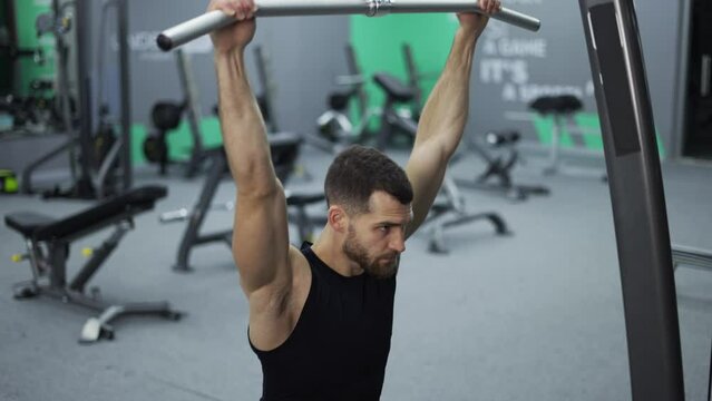 Male training back and hands muscles doing pulls weight exercise in a gym