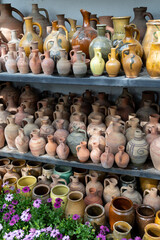 Fototapeta na wymiar Lot of handicraft ceramic pots with blooming plant flowers indoors. Many unique handmade colorful clay jugs and vases of various shapes on shelf in local Turkey market. 