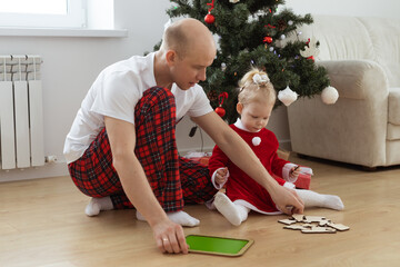 Toddler child with cochlear implant plays with father under christmas tree - deafness and innovating medical technologies for hearing aid