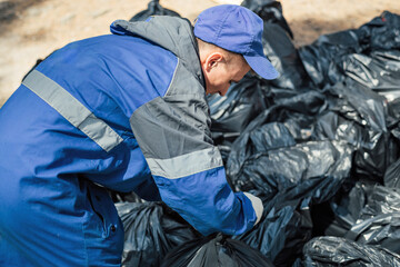 Man in overalls ties plastic bags of garbage. Ecological campaign of forest cleaning. Make nature cleaner. Volunteer cleans up garbage.