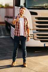 Portrait of young bearded man with thumbs up standing by his truck. Professional and positive truck...