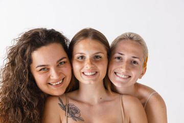 Portrait of three beautiful women posing together, smiling isolated over grey studio background