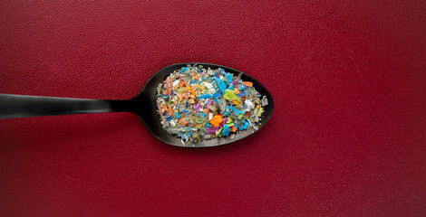 Close-up top shot on micro plastic particles in a spoon against dark red background. Concept for...