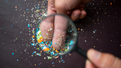 Close-up on micro plastic particles on the fingers under a magnifying glass. Concept for water...