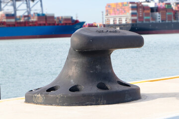 Sturdy metal mooring bollard at pier big black installed on concrete with a rope attached.  Used...