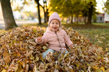 A little girl plays in a pile of autumn foliage.