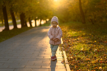 Fototapeta premium A girl in a pink jacket stands at sunset.