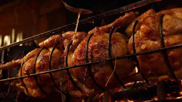 Roasted chickens on spit grilled over wood fire on big bbq barbecue with a spoon spilling sauce on it