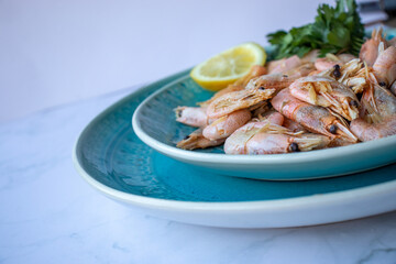 Сooked shrimp with parsley and lemon in a blue ceramic bowl on a white marble table background. Healthy Mediterranean seafood. Top view, flat lay, copy space
