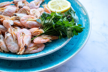 Сooked shrimp with parsley and lemon in a blue ceramic bowl on a white marble table background. Healthy Mediterranean seafood. Top view, flat lay, copy space
