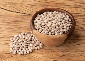 Raw brown beans in a wooden bowl over wooden table