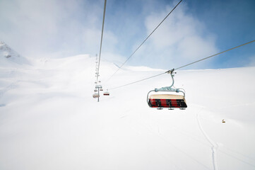 An open-air lift that goes to the top of the mountain for downhill skiing. Sunny day surrounded by...