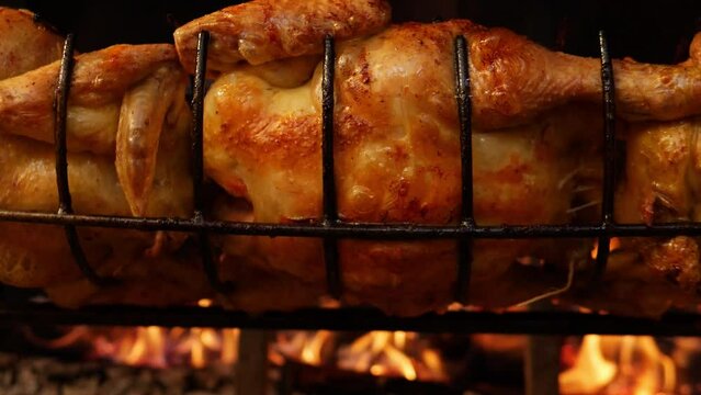 Slow motion closeup of a Roasted chickens on spit grilled over wood fire on big bbq barbecue 