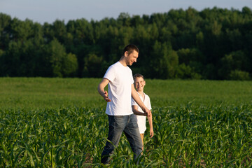 Naklejka na ściany i meble A cute boy walks in a cornfield with his dad and listens to him attentively