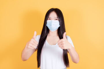 Asian woman wears white t-shirt in medical face mask to protect Covid-19 (Coronavirus) showing two double thumb up on yellow background