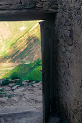 opened wooden door in the ruins of an abandoned house through which mountains are visible, in the ruins of the ghost village of Gamsutl in Dagestan