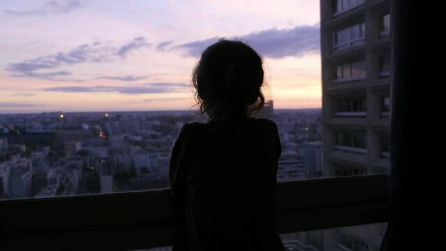A child watches the sunset from the window of his building, in Paris, France