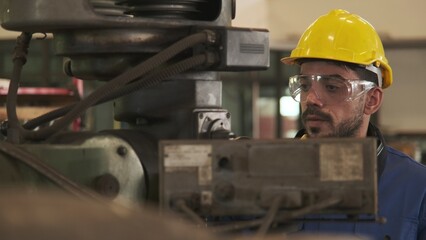 Factory worker wearing yellow hard hat and safety glasses inspect faulty machine.