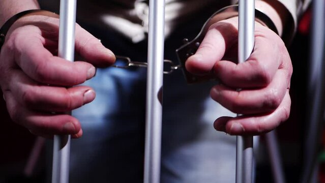 Prisoner in handcuffs reaches through prison bars