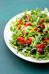 Summer delicious salad with arugula and fresh berries, red and black currants, sweet cherries and black mulberries, salad in an oval white plate on a green background