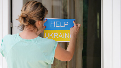 Woman glues banner on glass with the text help to Ukraine