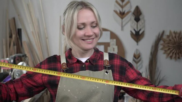 Woman in overalls worker with a construction tape measure. Portrait of a young woman carpenter at the workplace