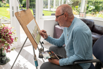 Portrait of  an active senior.  An artist painting with watercolours in his home studio.