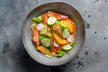 mixed salad with salmon and orange with sesame and greens top view on grey table