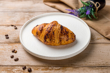 Croissant with chocolate on white plate on wooden table