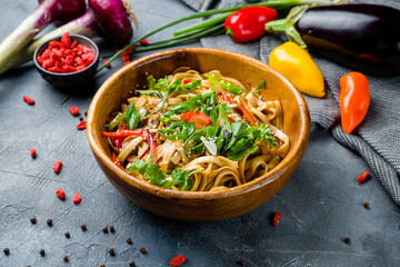 Udon noodles with vegetables on wooden bowl on grey table