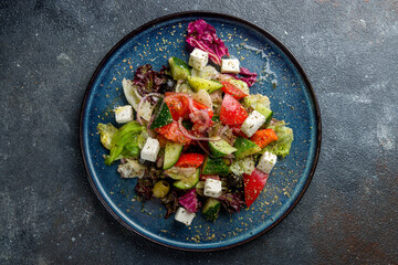 Greek salad with feta cheese and vegetables on blue plate on dark grey table top view