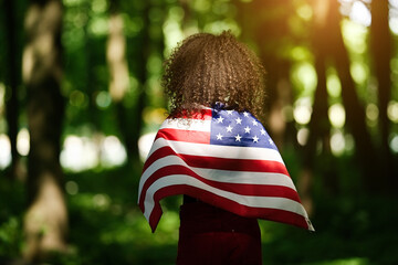 Young African american woman at nature background with an American USA flag on her shoulders. USA resident, US citizen. Immigration concept