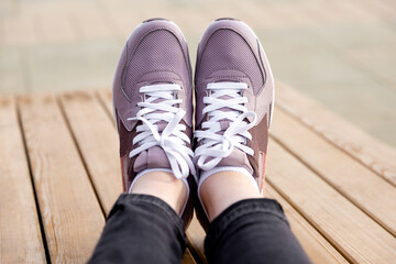 Womens legs in pink sneakers. Womens sports shoes on wooden planks. Side view