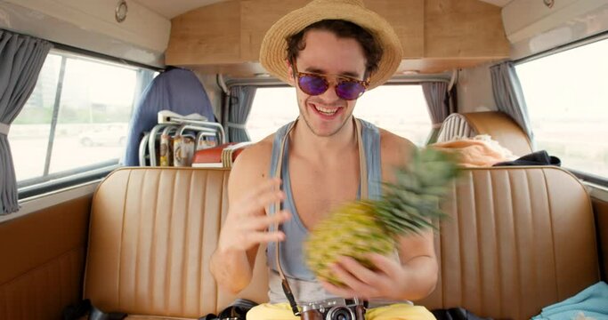 A young man having fun playing with a pineapple while taking photos in his camper van on vacation