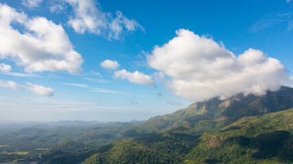 Aerial view of mountain peaks covered with clouds against the blue sky.