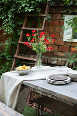 A bouquet of red poppies in a glass vase. Flowers in a vase at home. Interior Terrace, patio. Wooden table and plates for garden party or dinner. Table for lunch outside in garden in yard of house.	