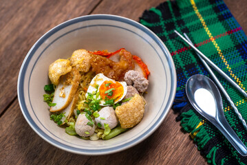 Spicy noodle with boiled egg and grilled red pork. Chinese egg noodles topping slice roasted pork, meatballon plate.