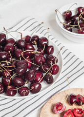 Fresh red cherries in a white plate on a white table. Sweet vegan dessert.