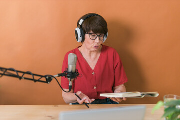 Portrait of mature woman wearing headphones and talking at online radio station - podcast and...